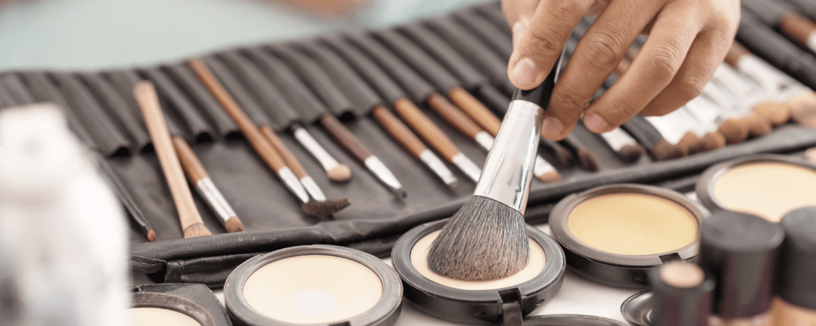 Makeup artist dabs brush in cosmetic powder to apply to client's face.