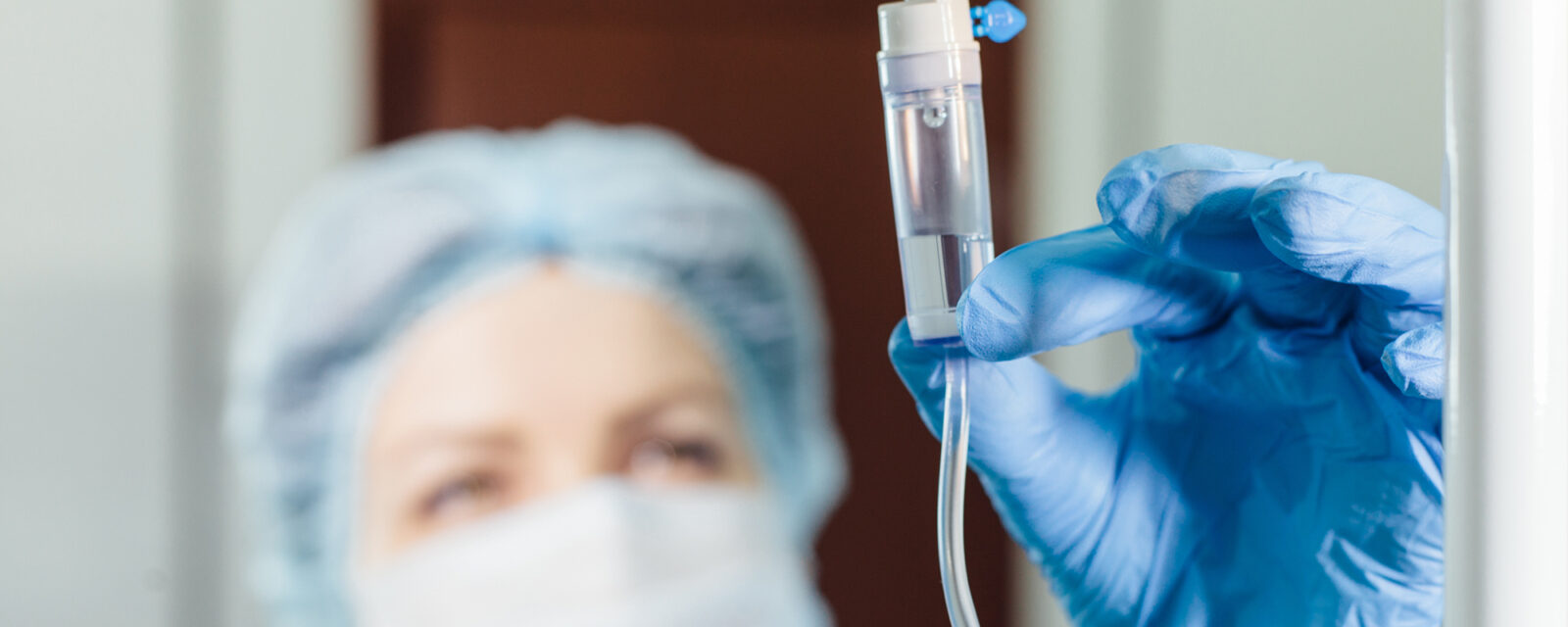 A female doctor wearing blue gloves and a blue hair net holding a container of chemotherapy medications.
