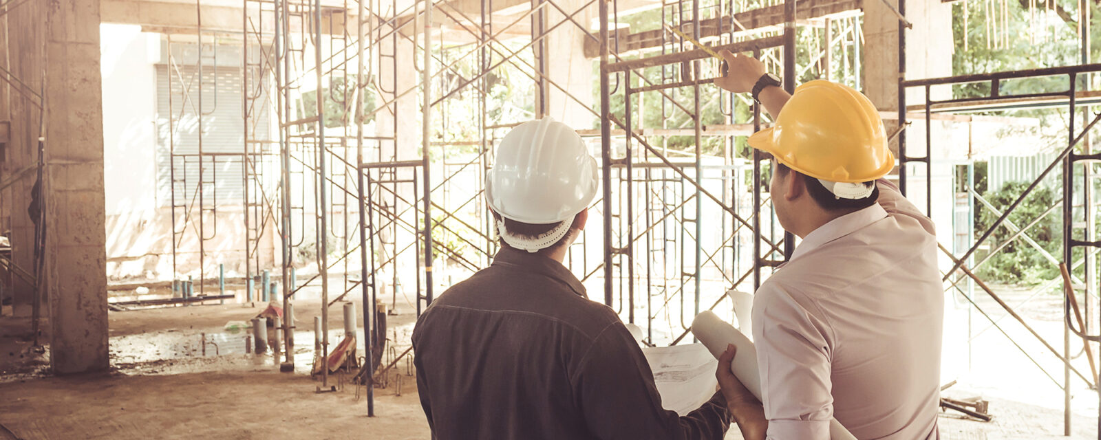 Image of two men in hard hats standing in a construction site. The man on the right is pointing at something in the distance.