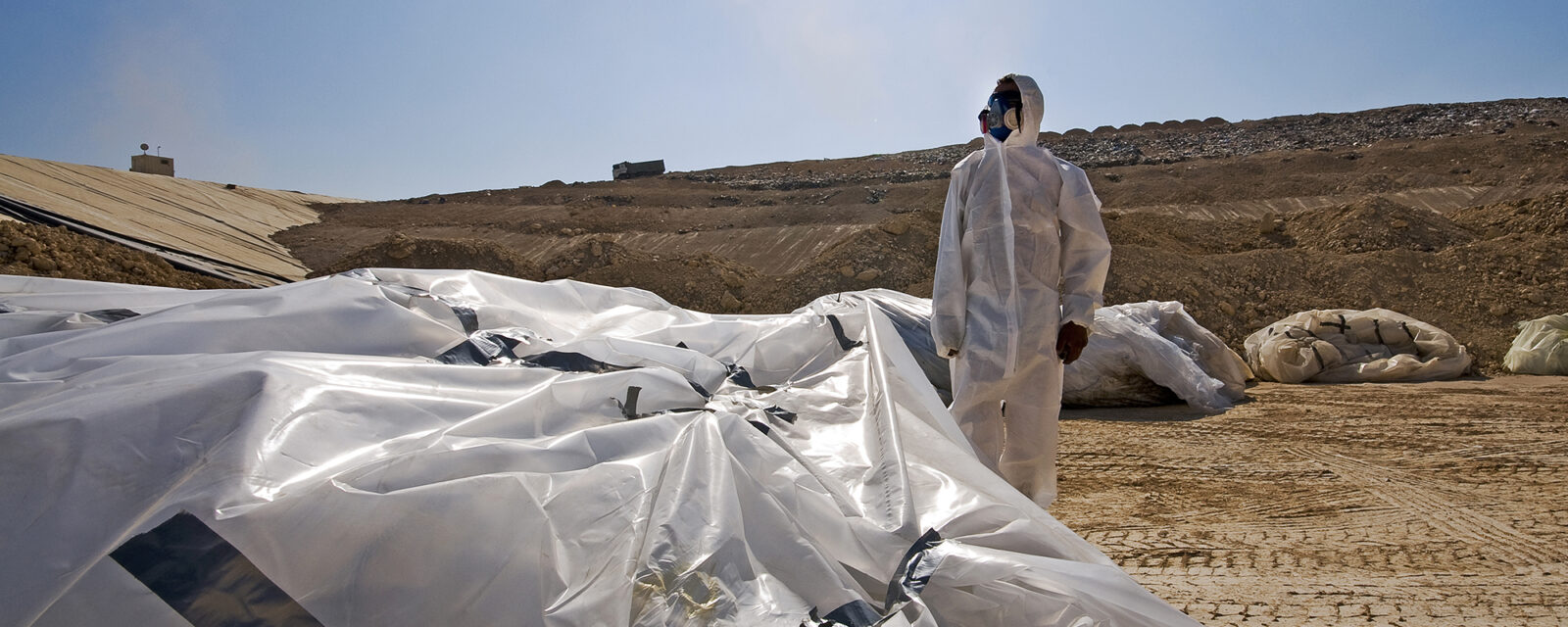 Image of an individual in a hazmat suit standing outside and looking off into the distance.