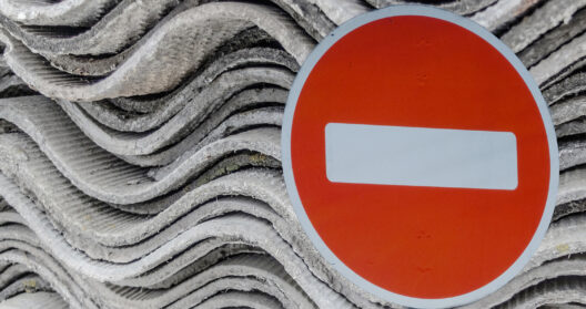 Image of a ban sign with asbestos-containing materials in the background.