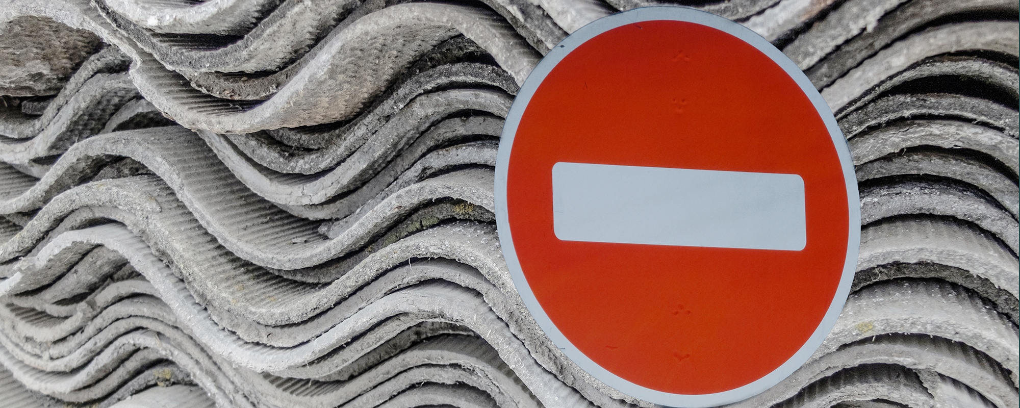 Image of a ban sign with asbestos-containing materials in the background.