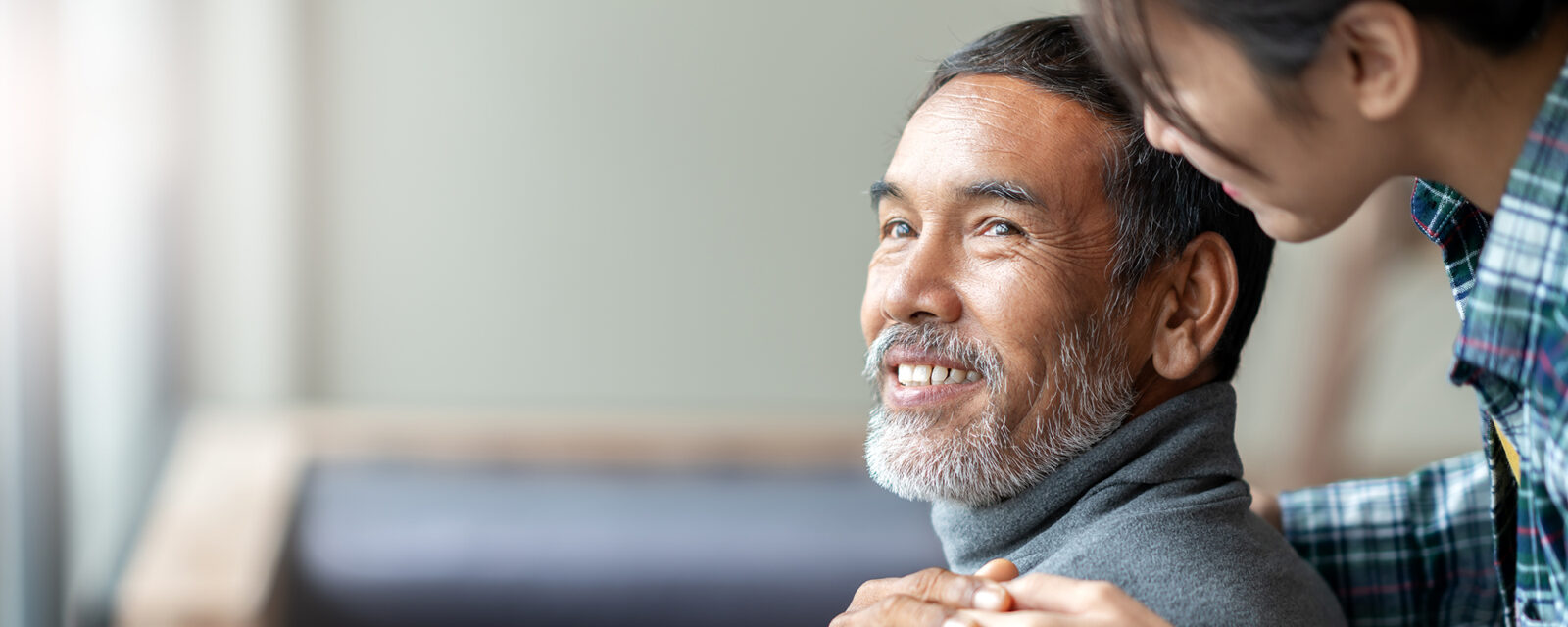 Image of a care giver behind her patient who is smiling and looking back at her.