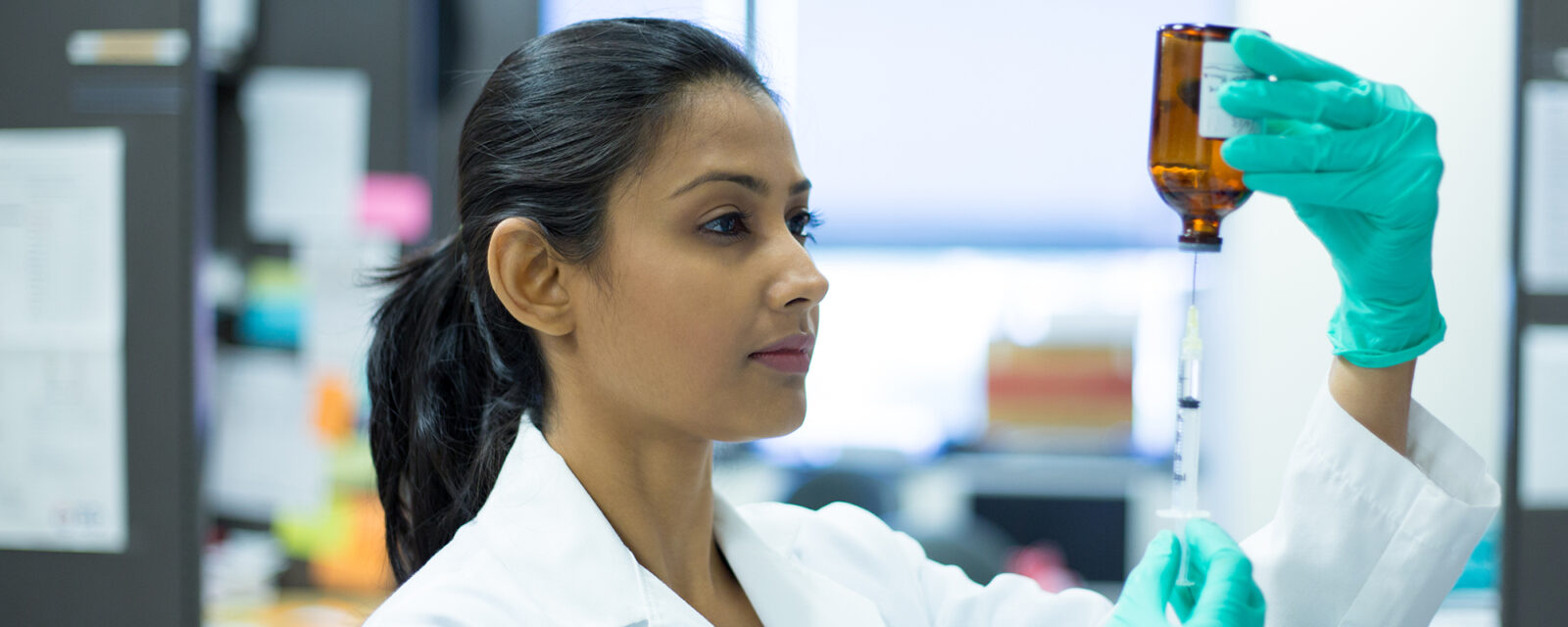 This is an image of a doctor working on a clinical trial in a lab. She is holding a bottle with a syringe connected to it.