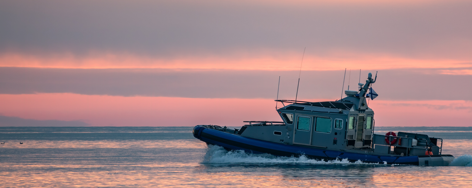 Image of a coast guard boat on the water with a sunset in the background.