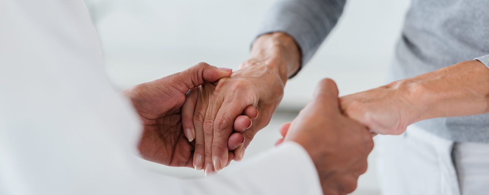 Close up image of a doctor holding the hands of his patient as a method of comfort after discussing the complications of a mesothelioma diagnosis.
