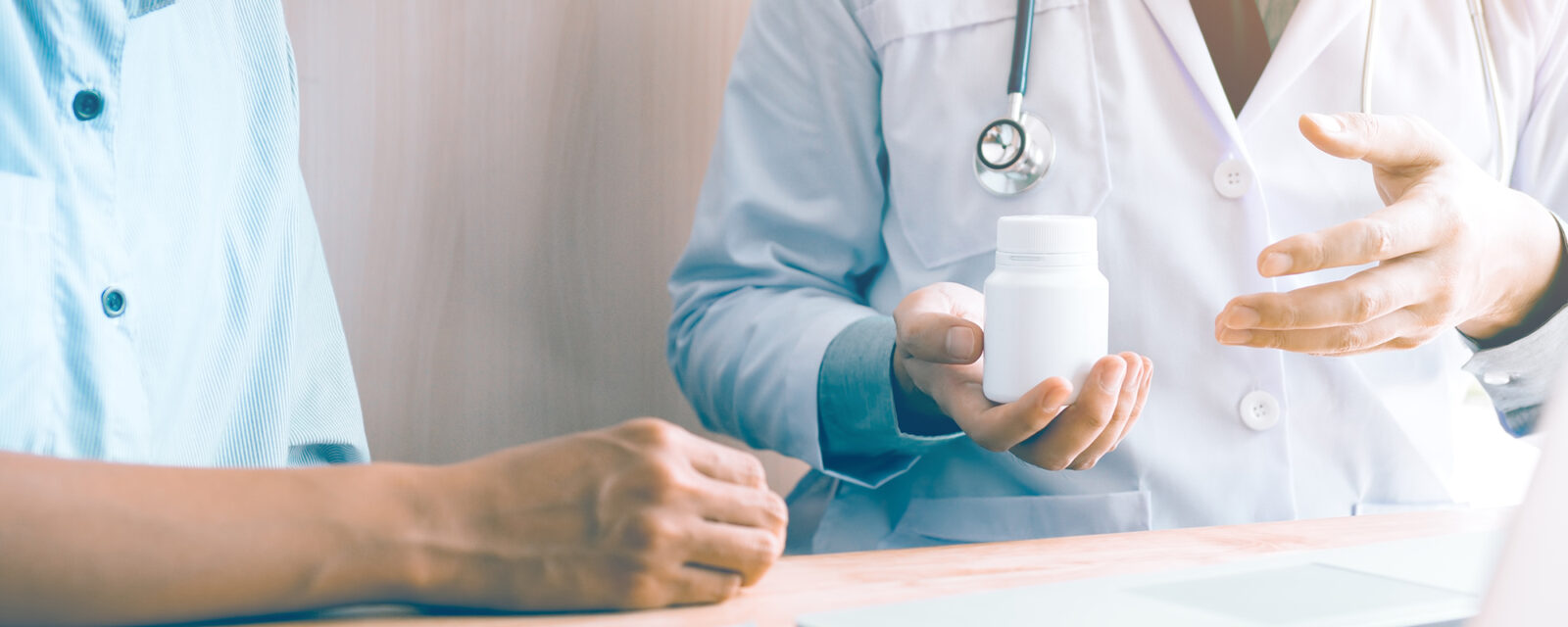 This is an image from the shoulders down of a doctor giving a patient a bottle of medication.