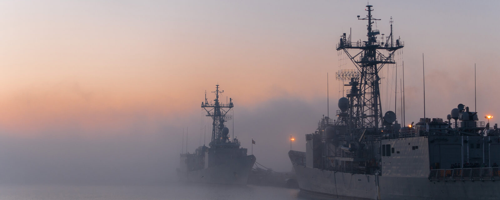 This is an image of two navy ships on duty and in the water with smog-filled air.