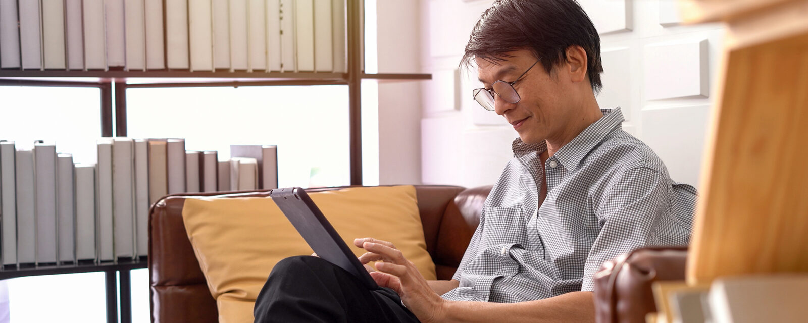 This is an image of a man sitting on a couch and looking at a tablet.