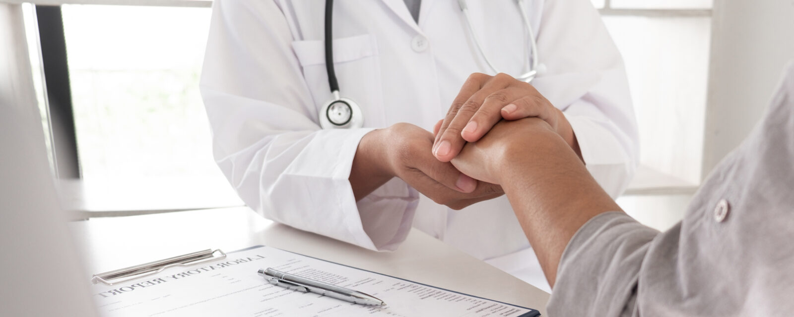 Close up image of a doctor holding their patient's hand as a method of comfort after explaining the effects of stage 3 mesothelioma.