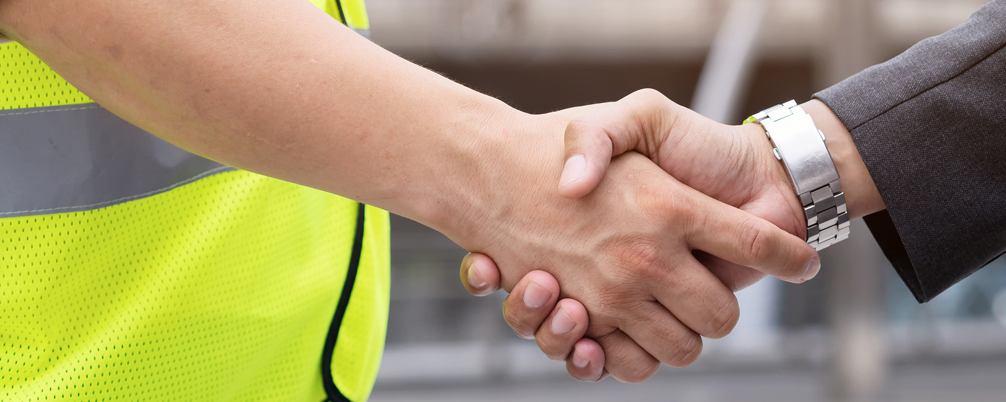 Close up image of a handshake between a business professional and a blue-collar worker.