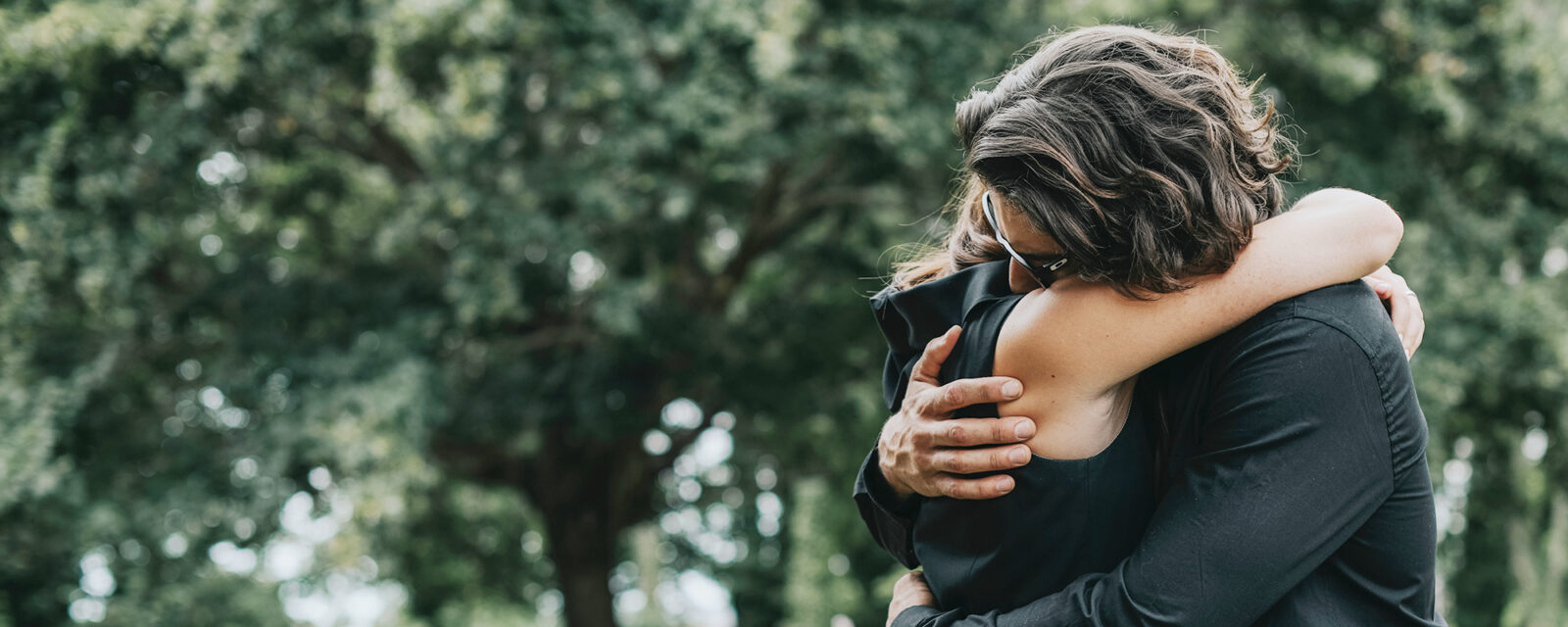 Image of two individuals wearing black and hugging while outdoors.