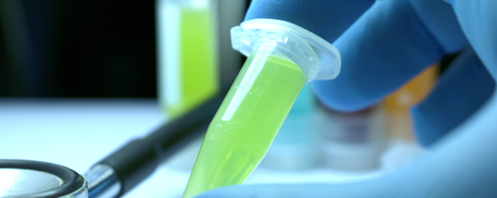 Image of a lab tech working with a droplet containing a bright yellow substance.