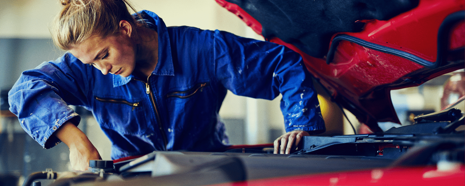 Image of a female automotive mechanic working on a car in a blue suit.