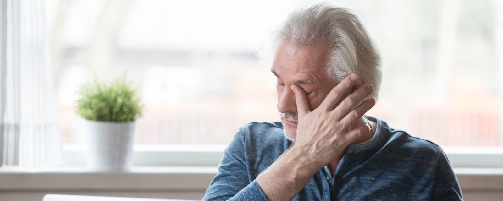 Fatigued mature old man taking off glasses suffering from tired dry irritated eyes after long computer use, senior middle aged male feels eye strain problem or blurry vision working on laptop at home