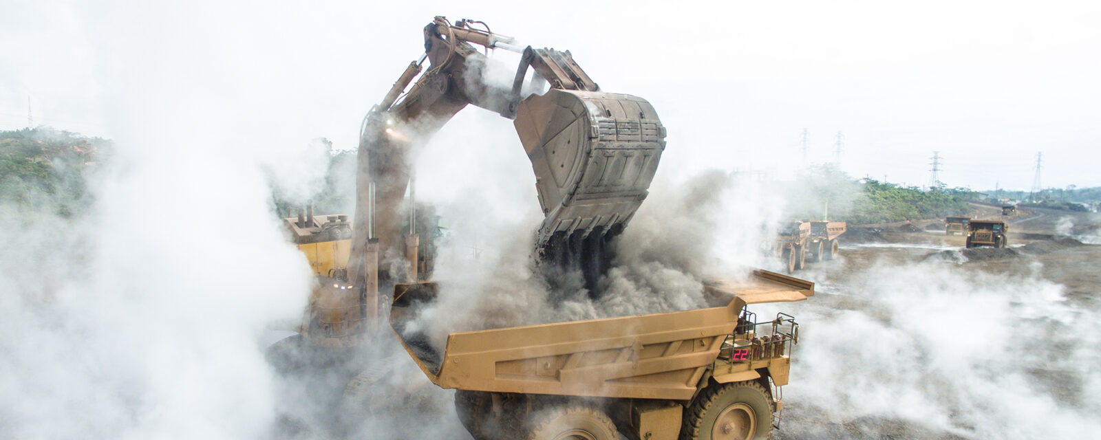 Backhoe load warm and smokey slag material into mining dump truck in Nickel Mining in South Sulawesi, Indonesia.