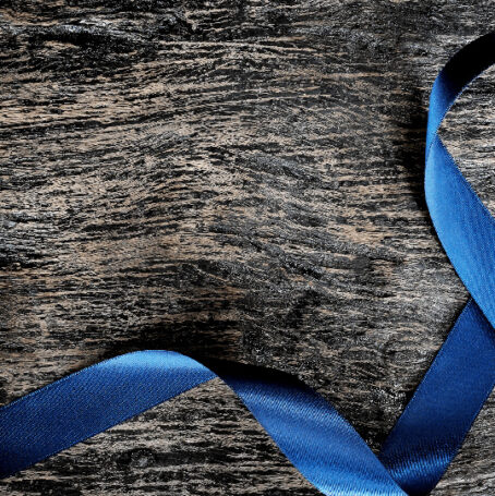 Image of a blue ribbon, representing cancer patients, lying on a wooden table.