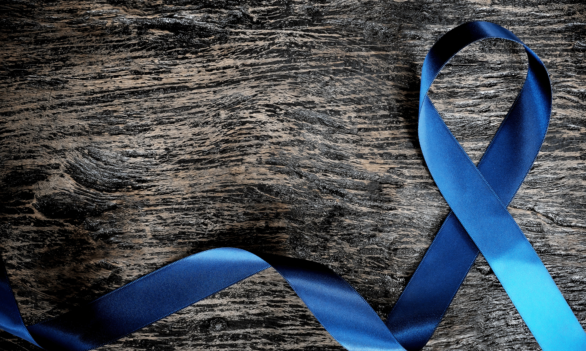 Image of a blue ribbon, representing cancer patients, lying on a wooden table.