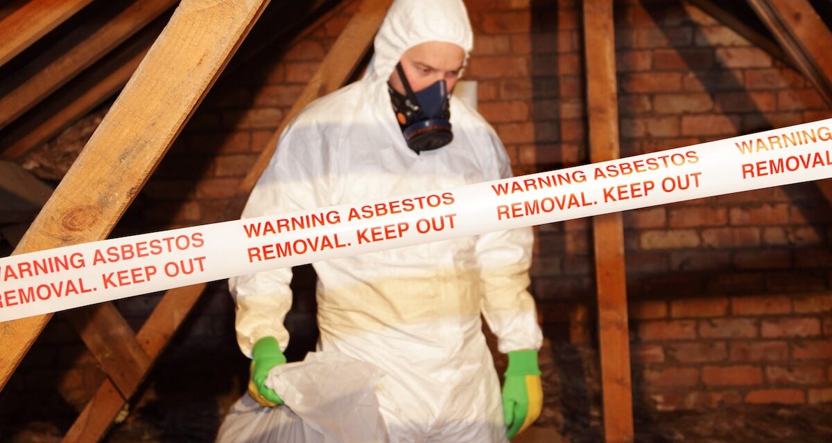 Man removing asbestos from attic in full PPE gear