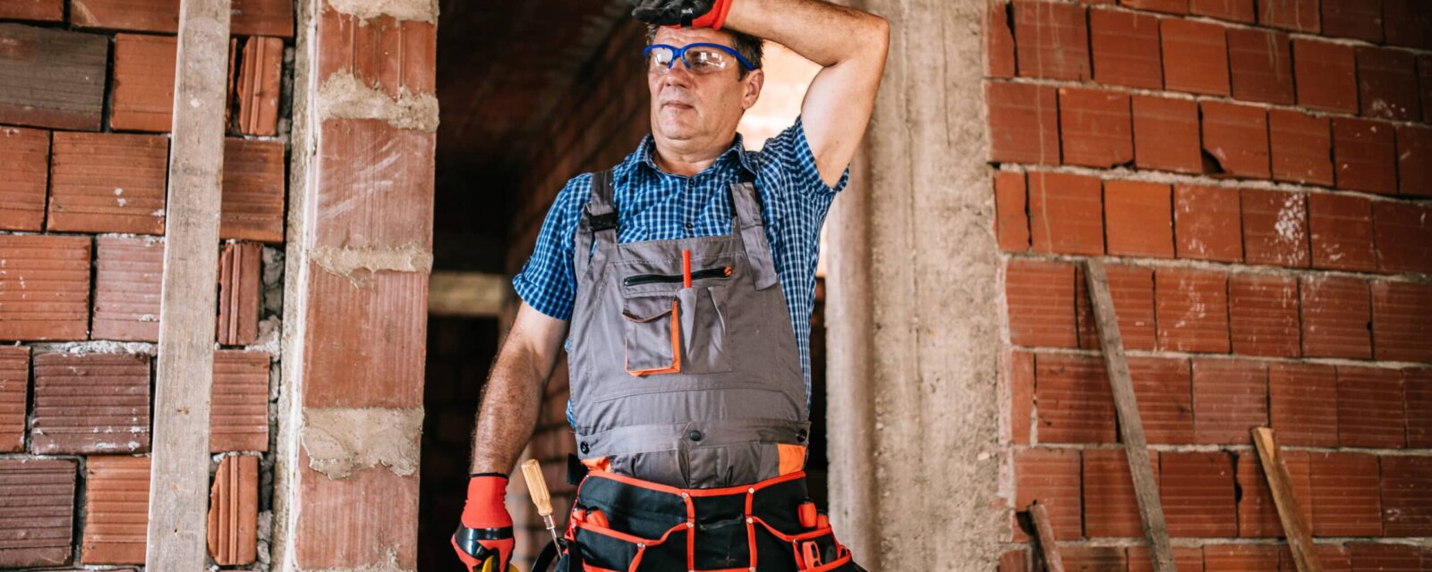 Construction worker with his arm on his forehead as if he is wiping off sweat. He is visually exhausted.