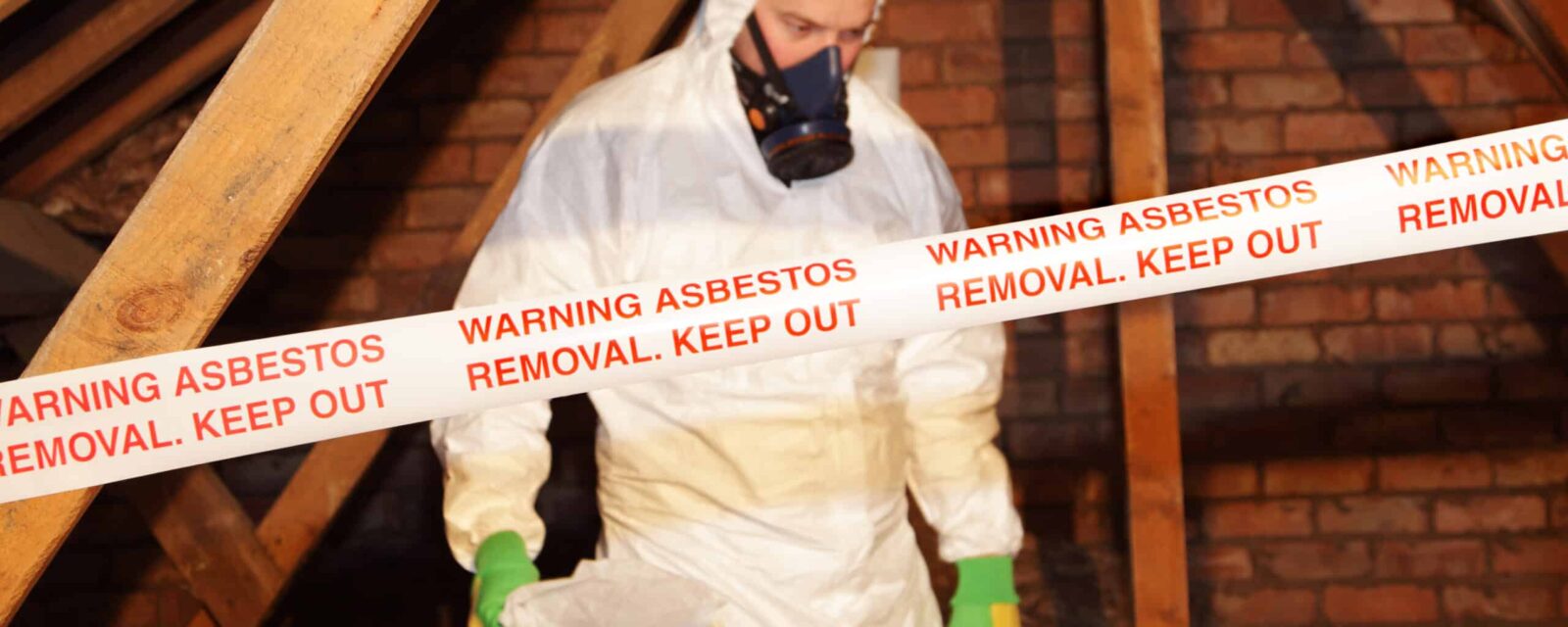Young man in hazmat suit removing asbestos with a warning keep out sign.
