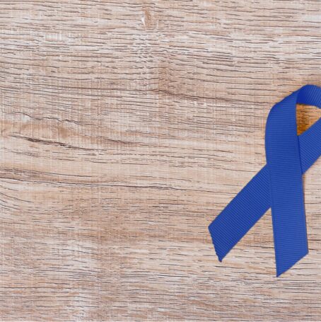 Blue ribbon for mesothelioma awareness lying on wooden desk.