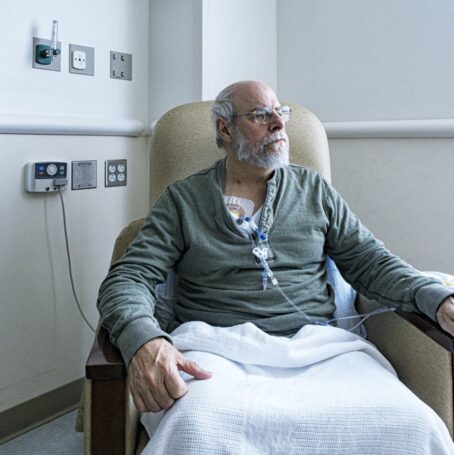 Male patient with glasses sitting in treatment chair and receiving chemotherapy treatment.