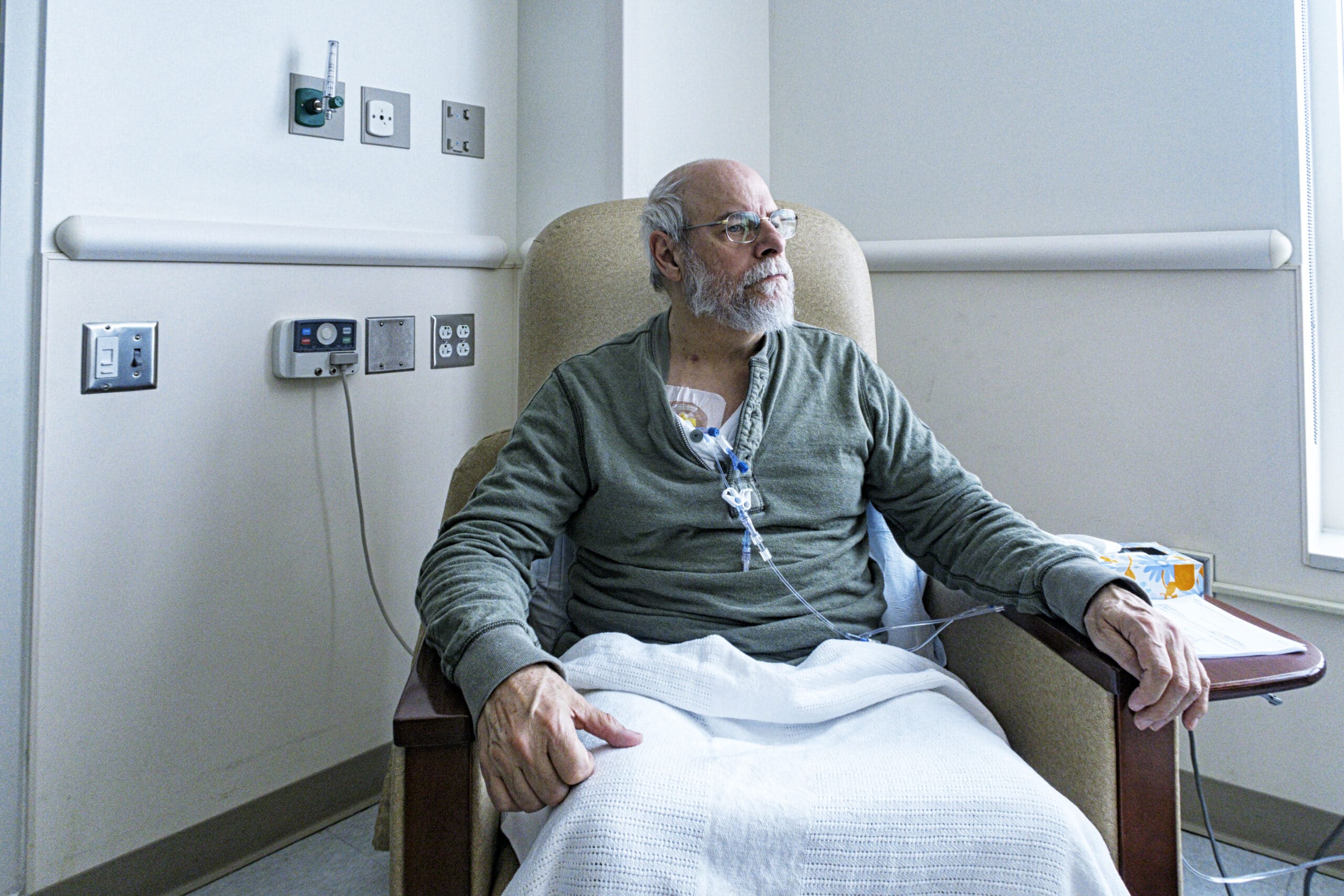 Male patient with glasses sitting in treatment chair and receiving chemotherapy treatment.