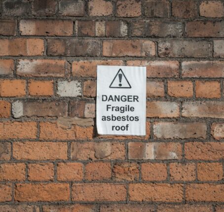 Asbestos sign outside of a school on a faded brick wall.