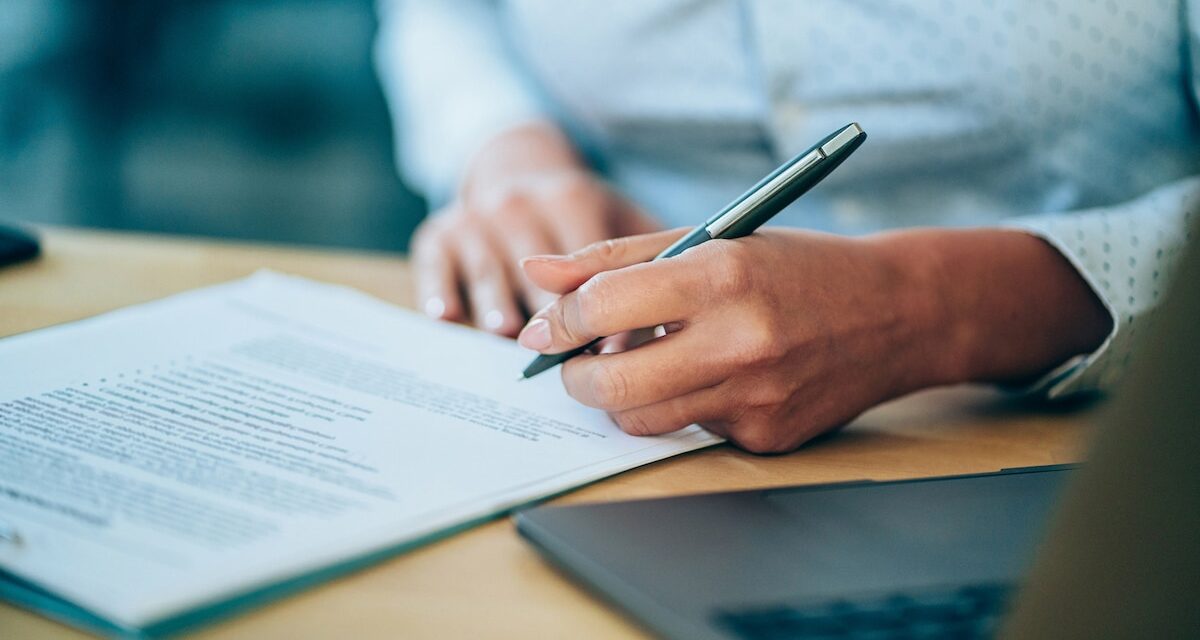 Image of client holding pen and signing legal contract.