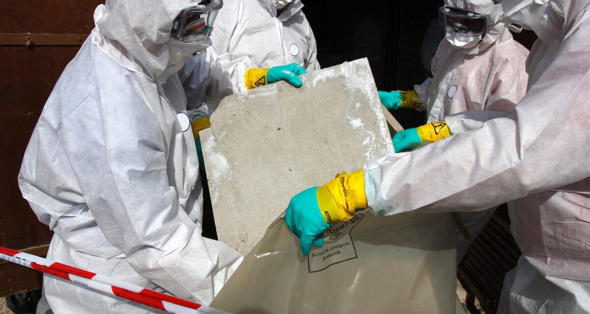 Asbestos abatement crew bags debris in full personal protective equipment gear.