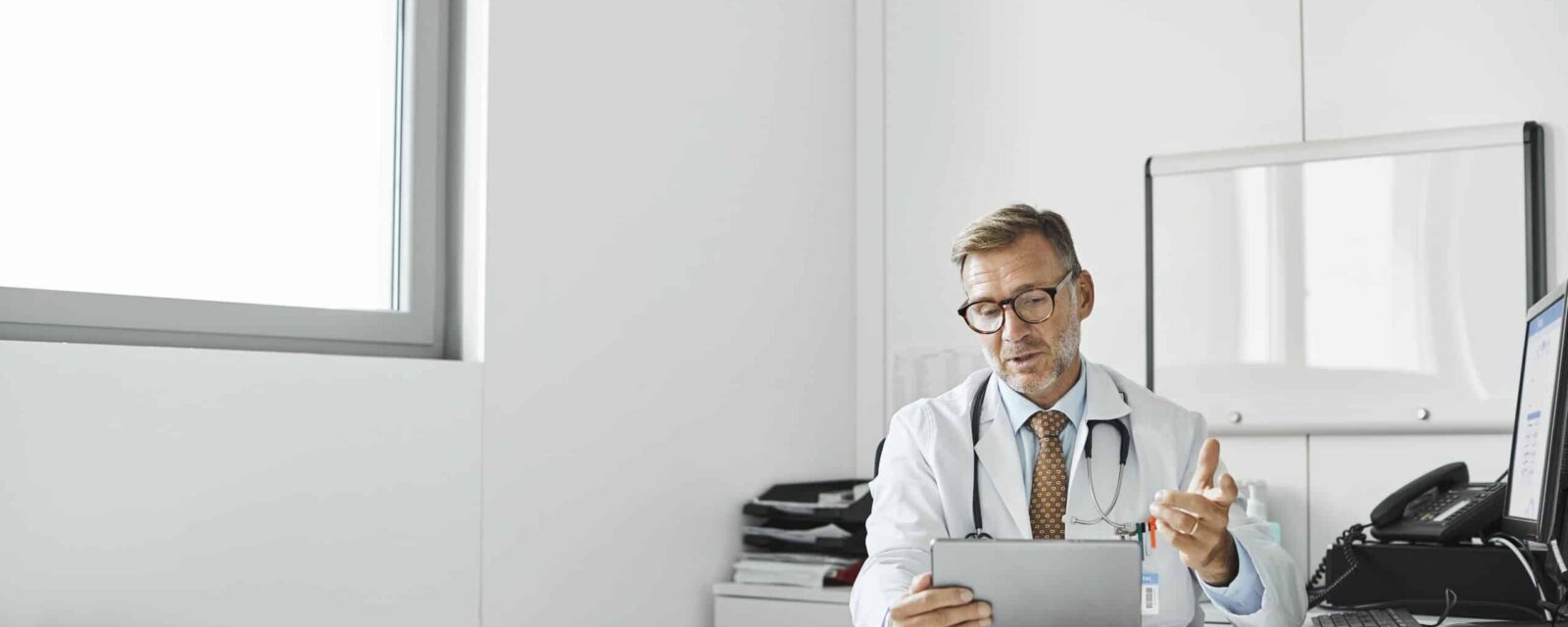 Mesothelioma doctor sitting at desk and looking at information on tablet.