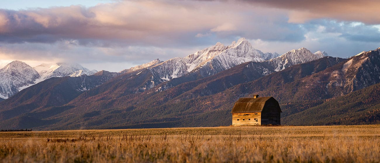 Image of barn with empty field and mountains in the background in Montana.
