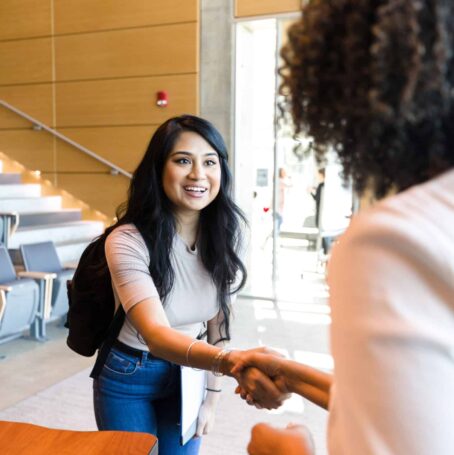 College student eagerly shakes the hand of their professor at a university.