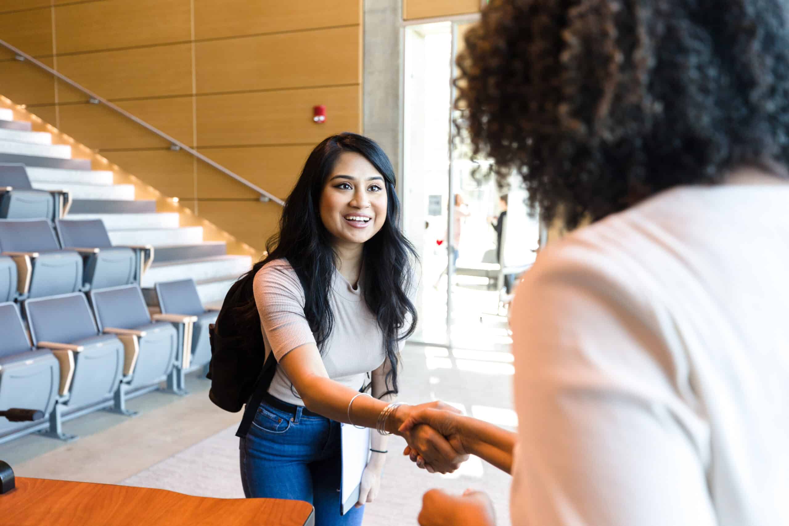 College student eagerly shakes the hand of their professor at a university.