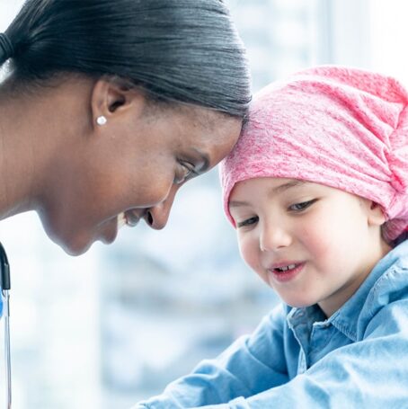Female oncologist touching foreheads with a little girl.