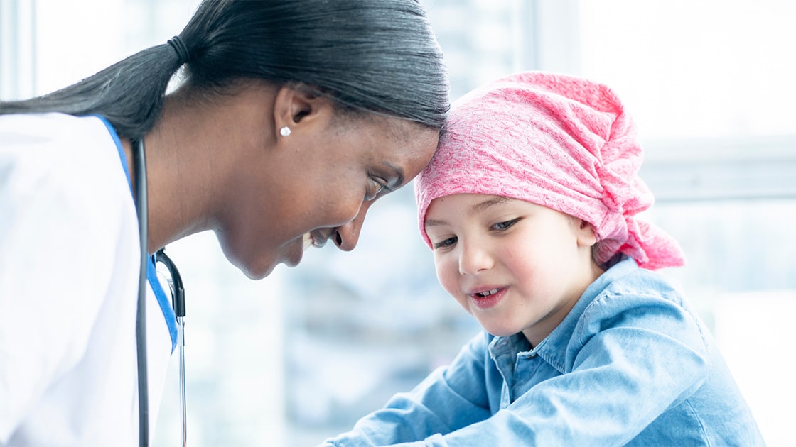 Female oncologist touching foreheads with a little girl.