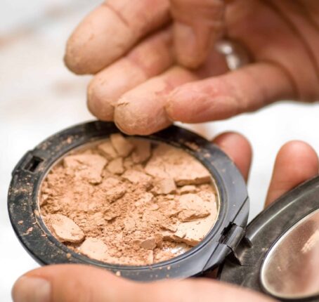 A shattered cosmetic product and a person's fingers touching the item. MoCRA law adds more guidelines and restrictions to cosmetics products.