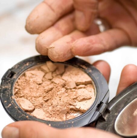 A shattered cosmetic product and a person's fingers touching the item. MoCRA law adds more guidelines and restrictions to cosmetics products.