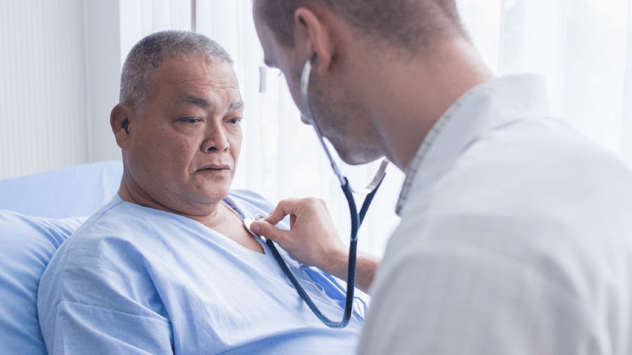 Young male doctor using stethoscope to listen to heartbeat of old male patient.