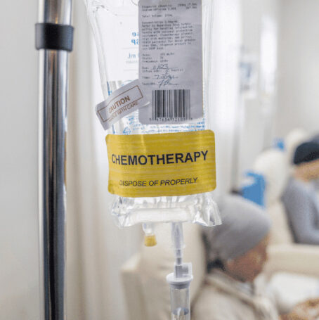 An intravenous bag on chemotherapy hangs from an IV pole as three cancer women dressed comfortably receive cancer chemotherapy treatment despite the chemotherapy drug shortages.