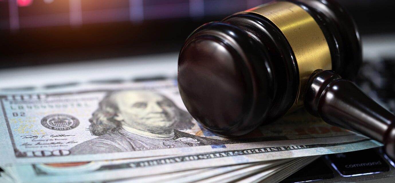 Close up of gavel laying on top of hundred-dollar bills.