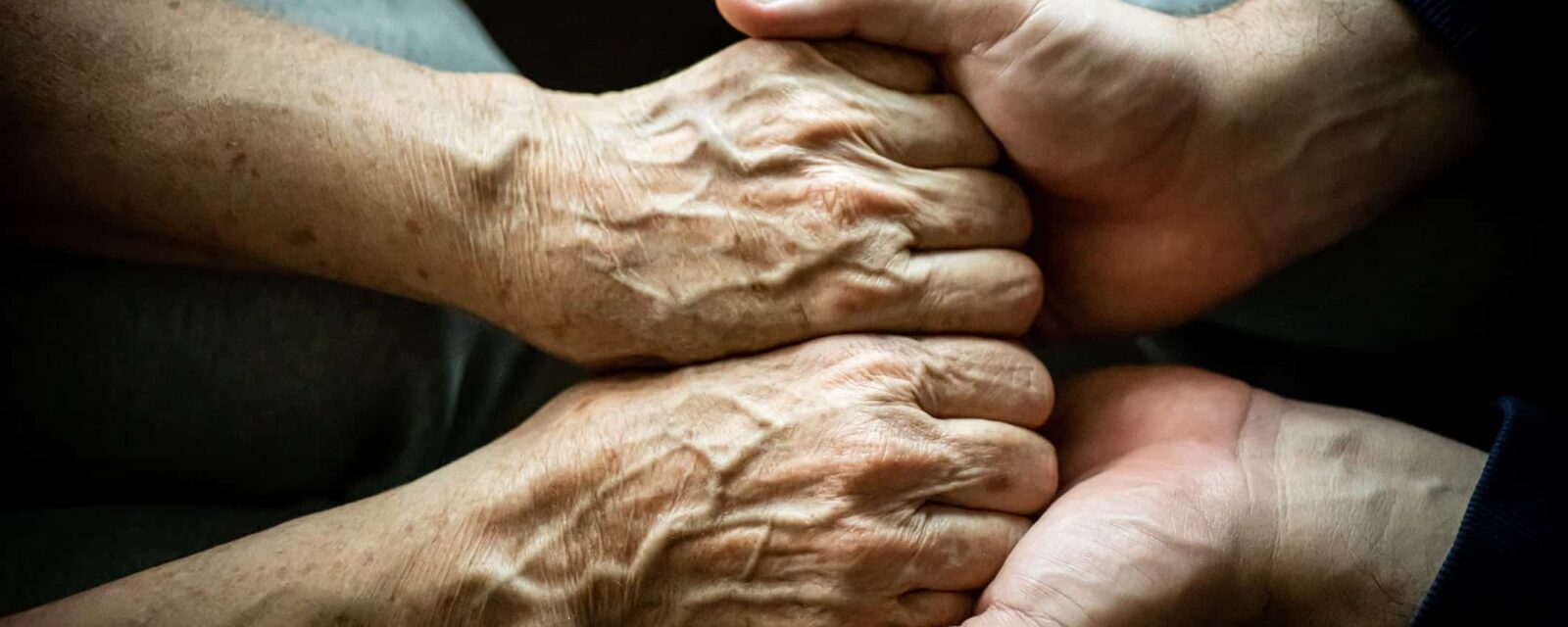 Photograph of elderly person's hands holding young person's hands while conveying anticipatory grief.