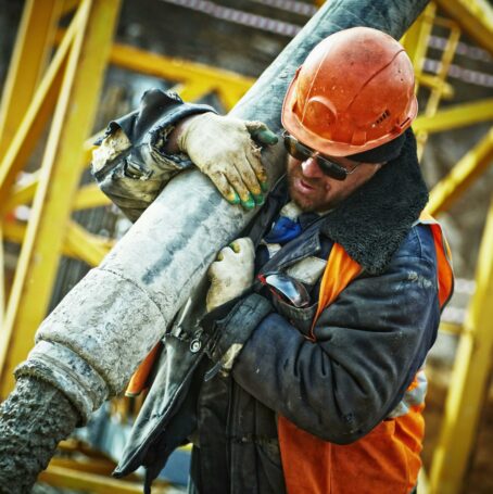 Construction workers wearing hard hat and gloves carrying asbestos cement pipe while in the workplace.