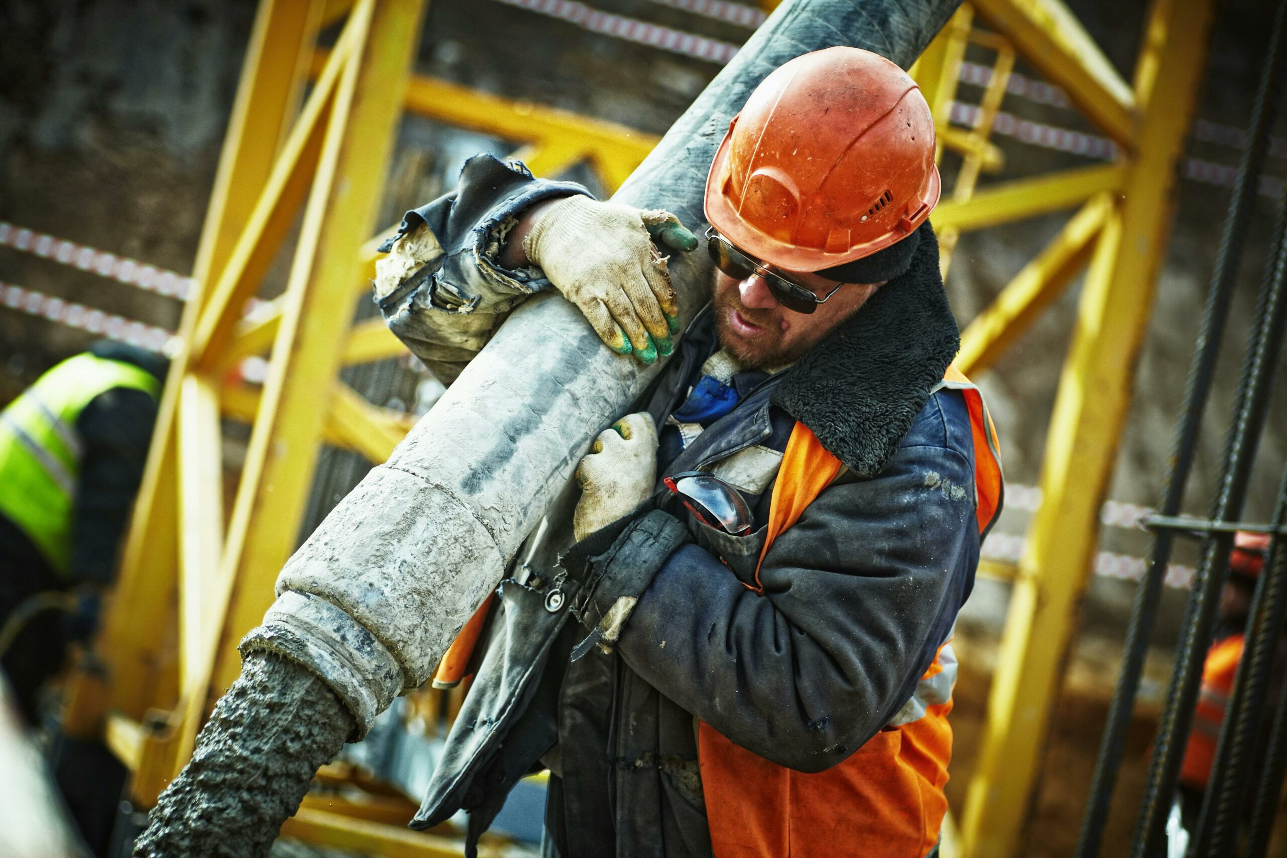 Construction workers wearing hard hat and gloves carrying asbestos cement pipe while in the workplace.