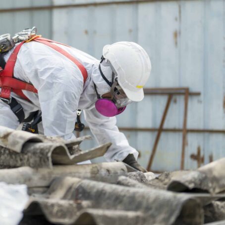 Workers wearing protective clothing while removing the asbestos roof. Hazardous waste management and working safety concept. Professional waste disposal.