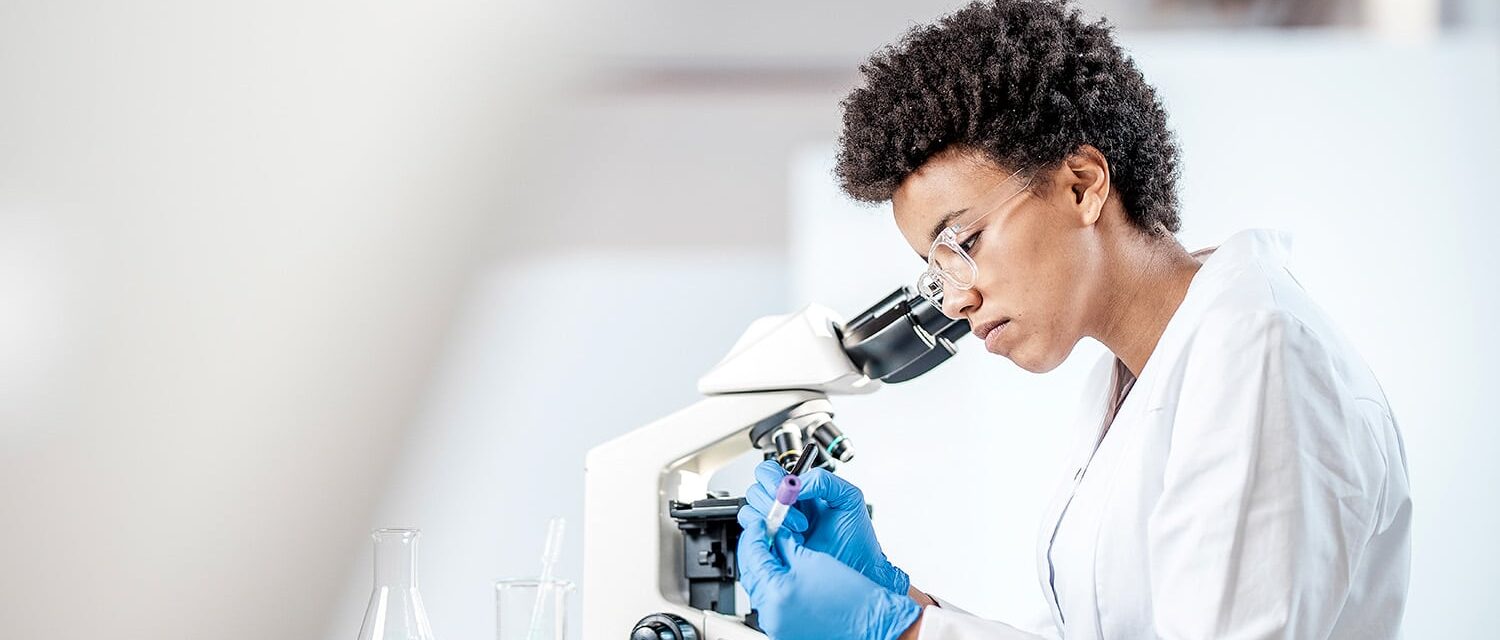 Lab technician looking at test tube samples through microscope.