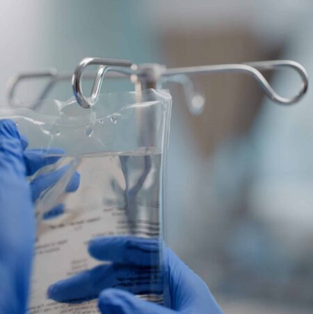 Hands, IV drip, and saline solution in hospital, clinic and healthcare facility for health and healing. Doctor, nurse and closeup of medical equipment for intensive care, life support and medicine