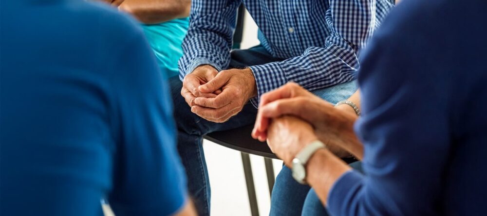 Group of three people with their hands held together during a mesothelioma support group session