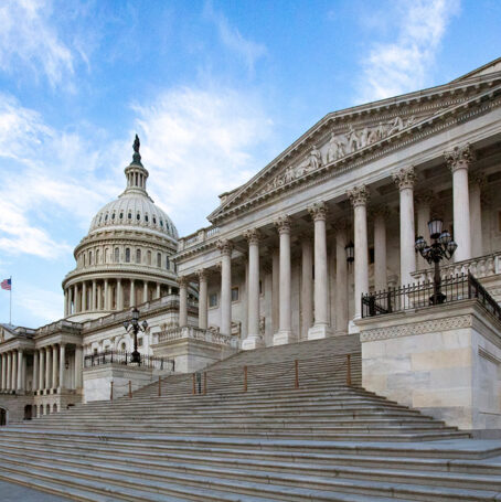 Exterior view of the United States Capitol building in Washington, D.C., featuring the white dome, grand marble steps, and neoclassical columns.